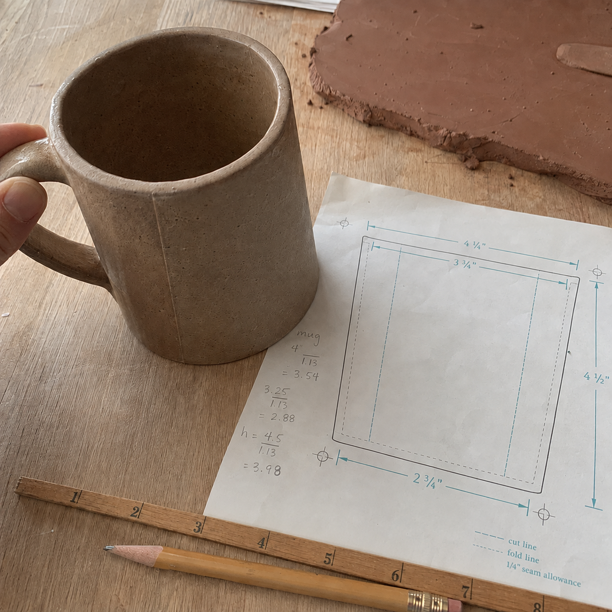 Handbuilt mug next to its paper template, shrinkage test tile, ruler, and pencil